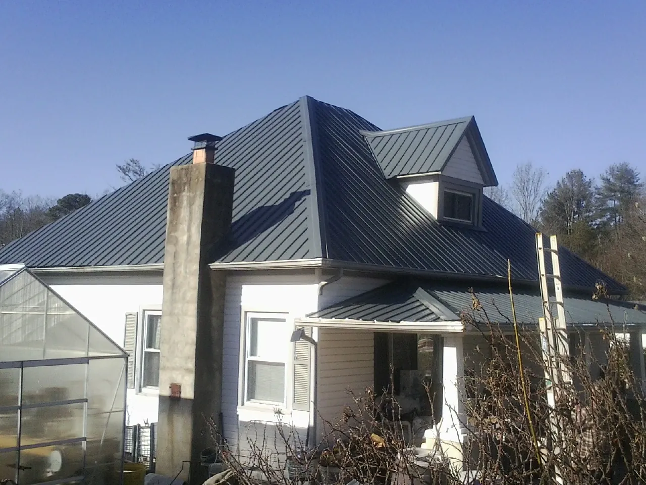 Dark blue standing seam metal roof on a white farmhouse with dormer — Slate & Tile Roof Repair by Roofing Brothers in Middlebranch