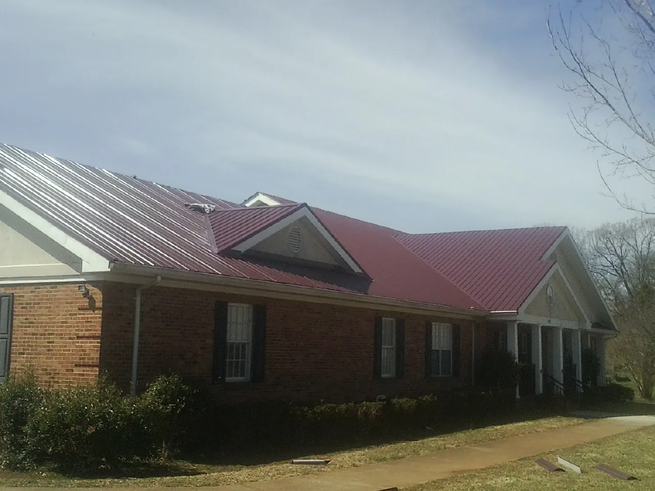 Red metal roof with gabled entries on a long brick building, from a Hail Damage Roof Repair job in Middlebranch