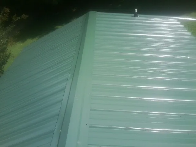 New green metal panels meeting at the ridge of a roof — Flat Roof Repair work by our crew in Middlebranch