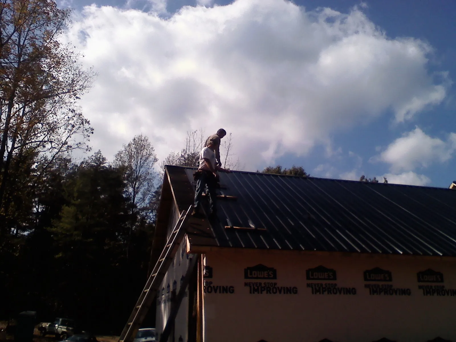 Roofer fastening dark metal panels high against a cloudy sky, from a Roof Inspection job in Middlebranch