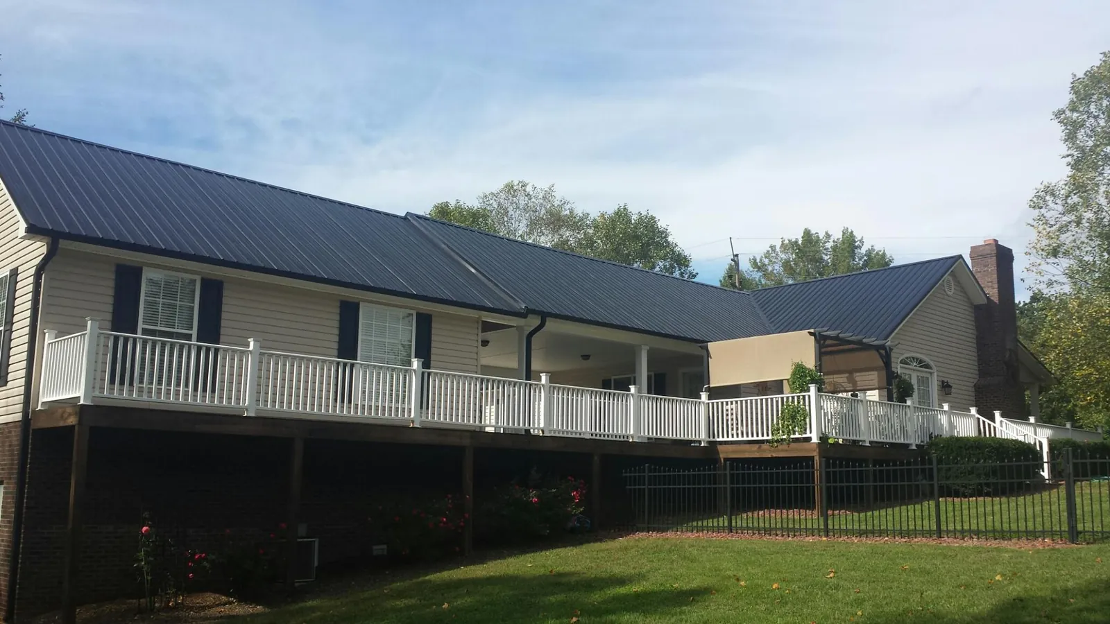 Black metal roof above a long white railed deck on a hillside home in Middlebranch