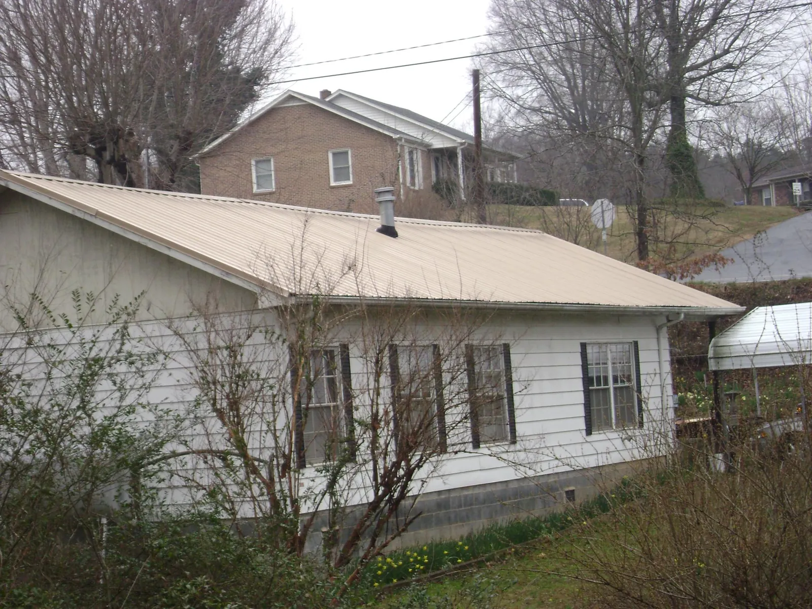 Tan metal roof on a white sided house set into a hillside — Commercial Roofing by Roofing Brothers in Middlebranch